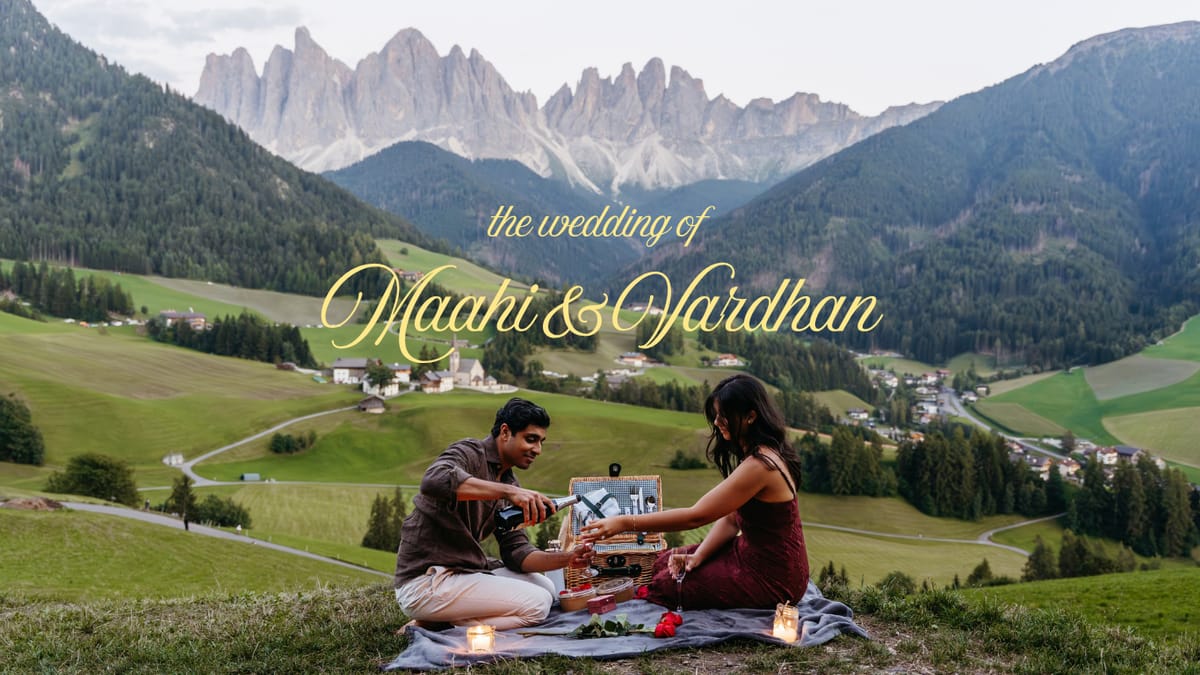 The wedding of Maahi and Vardhan. The two of them sit on a blanket on a hillside at dusk, pouring a drink from a picnic hamper, with an alpine village in the valley below and jagged peaks behind.